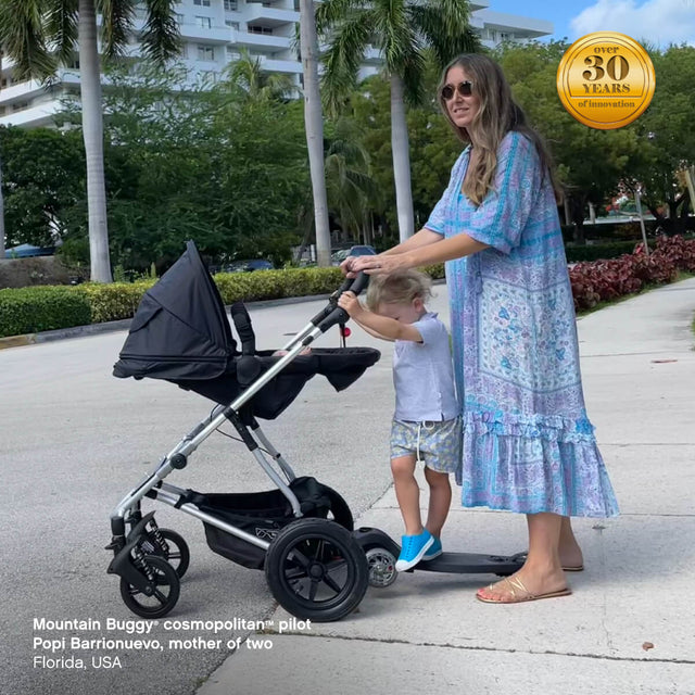 mother of two pushing cosmopolitan stroller in parent facing position with freerider™ scooter attached - Mountain Buggy cosmopolitan™ pilot Popi Barrionuevo, Florida, USA - fabric colour_black