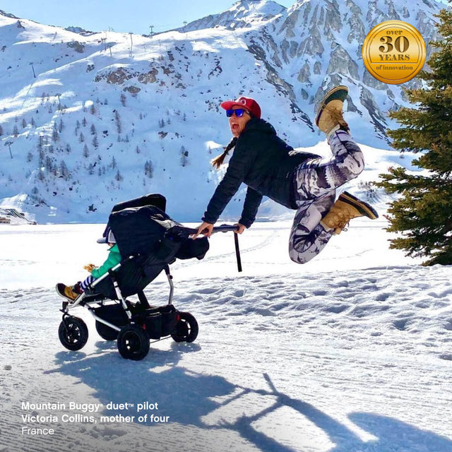 active mom pushing duet double stroller while jumping for joy at the snow field - Mountain Buggy duet™ pilot Victoria Collins, mother of four, France