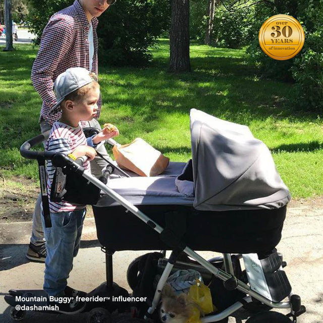 family strolling through park with toddler riding their freerider™ scooter board attached to rear of duet™ double stroller - Mountain Buggy freerider™ influencer @dashamish
