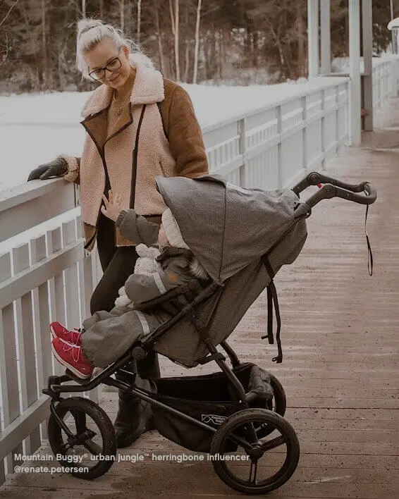 Winter snow boardwalk with mum talking to toddler sitting snug in the urban jungle buggy with herringbone fabric as part of the luxury collection from Mountain Buggy