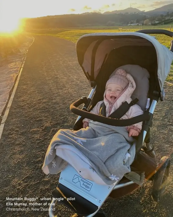 Happy baby sitting in 3 wheel all-terrain pram with hat and blanket at sunset - Mountain Buggy