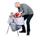 phil&teds carrycot stand with storage basket and nest baby bassinet on top and father taking baby out of bassinet 3/4 view